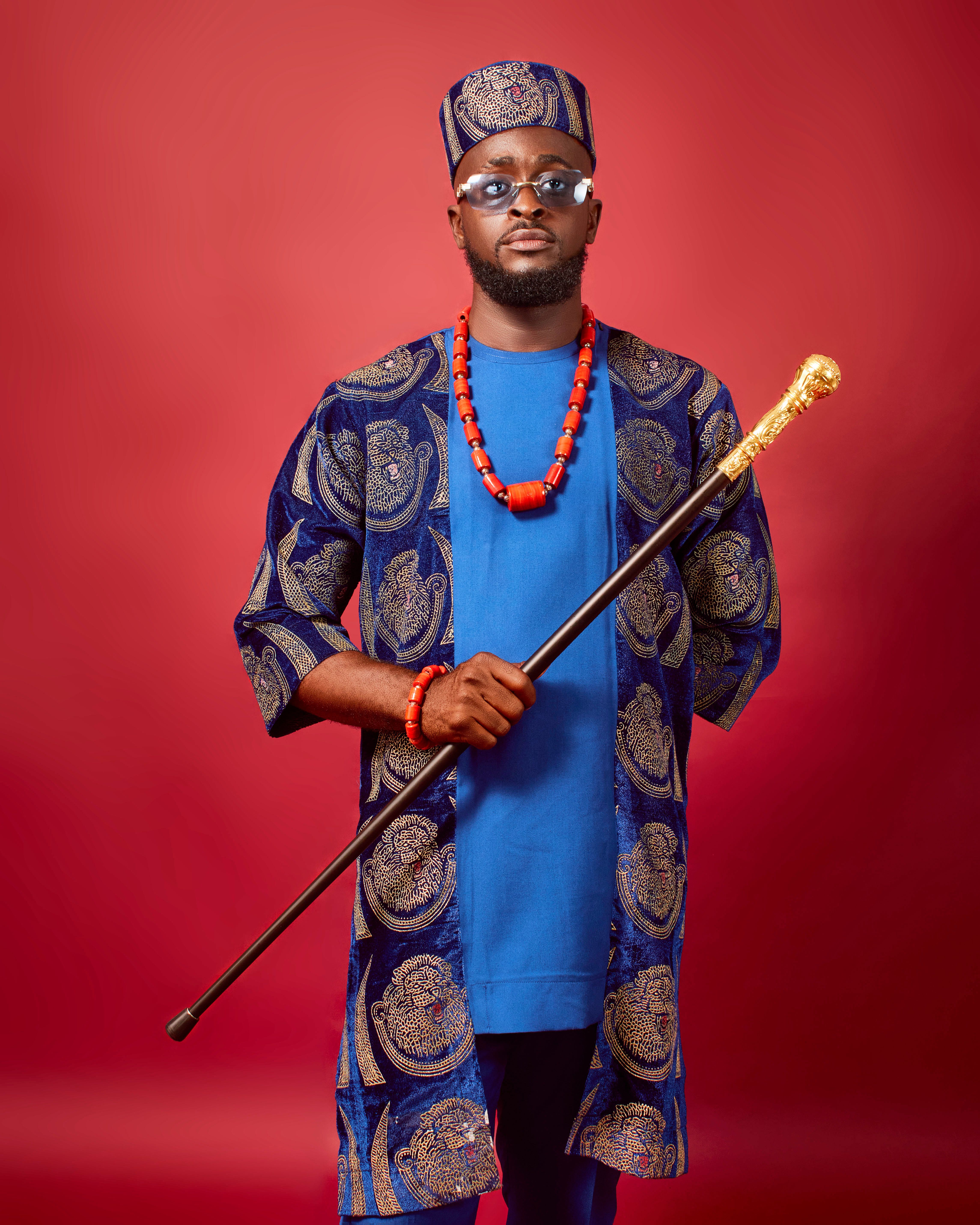 African man wearing traditional attire with a cane, striking a confident pose.