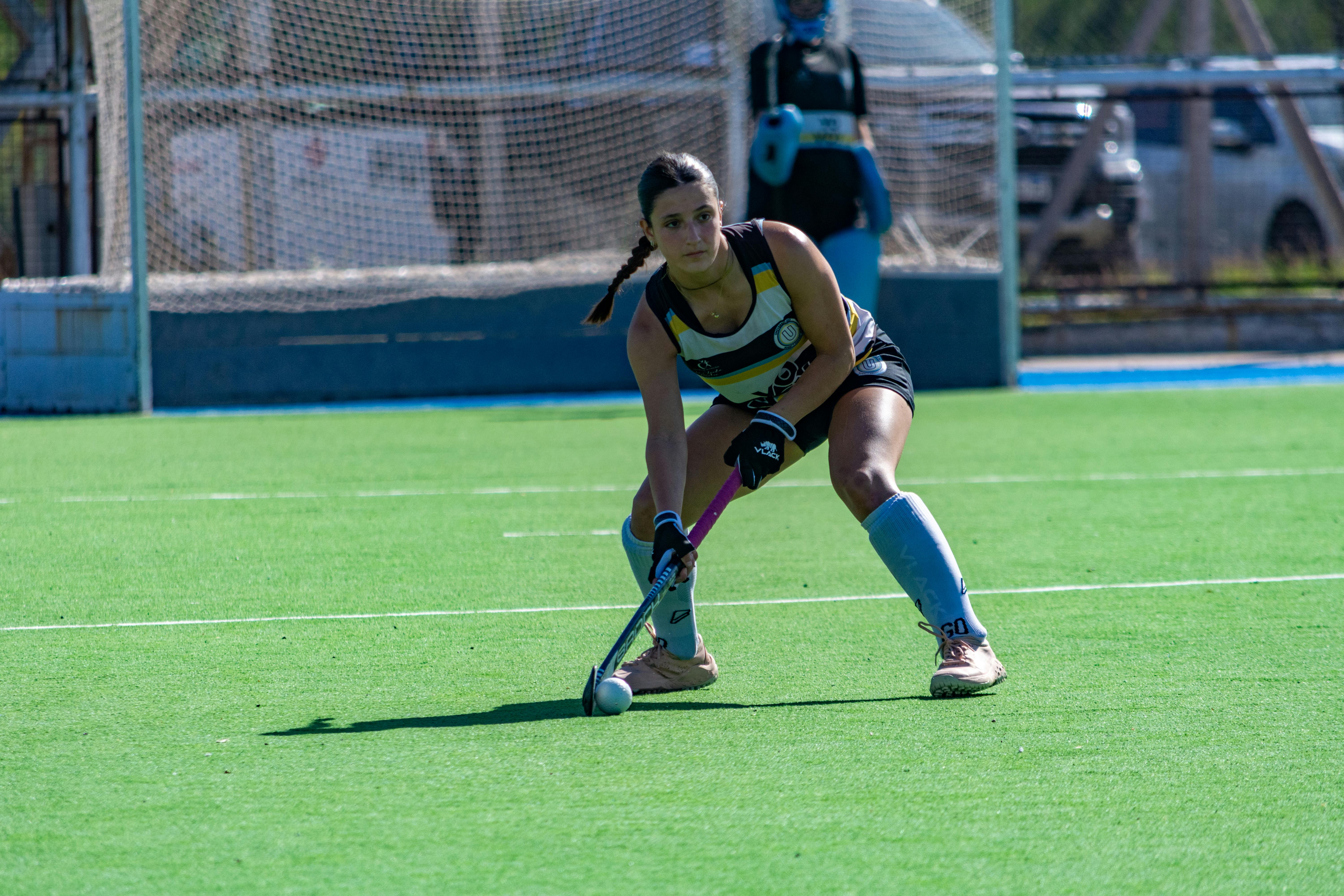Focused female field hockey player poised to strike on a sunny outdoor field.