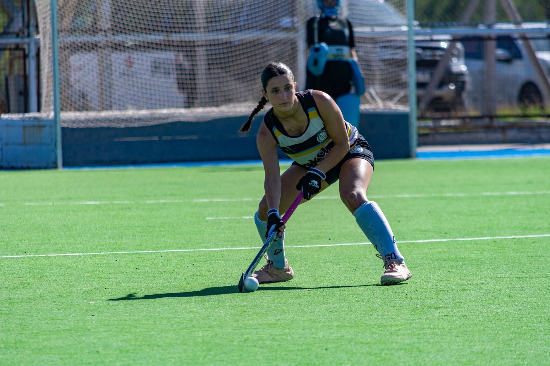 Focused female field hockey player poised to strike on a sunny outdoor field.
