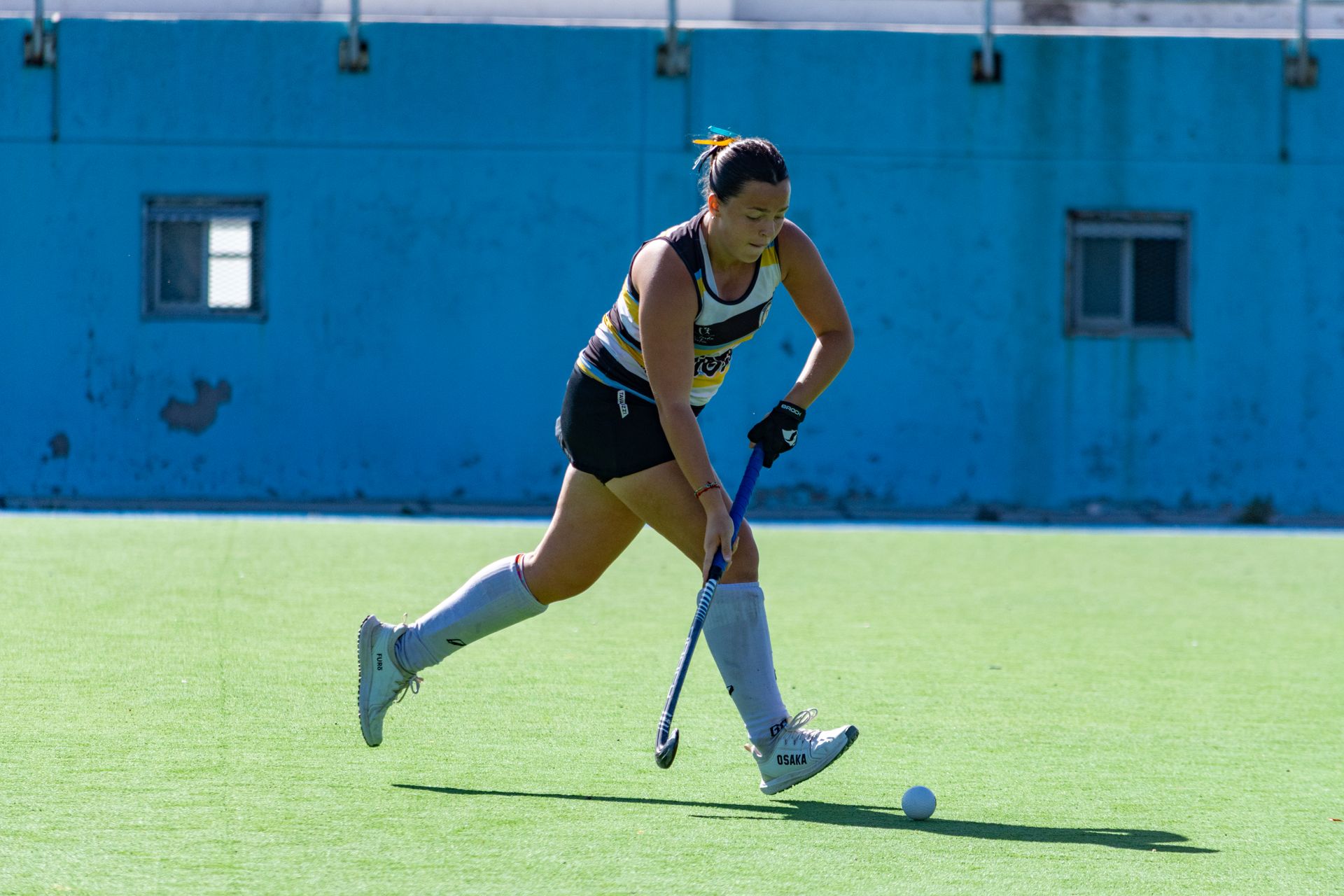 A female field hockey player focused on the game during a sunny day outdoors on the field.