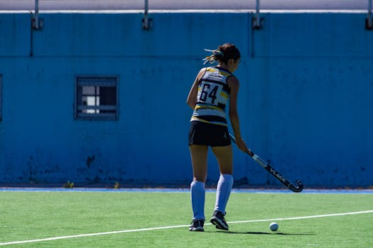 A female field hockey player on a bright outdoor field during the day.