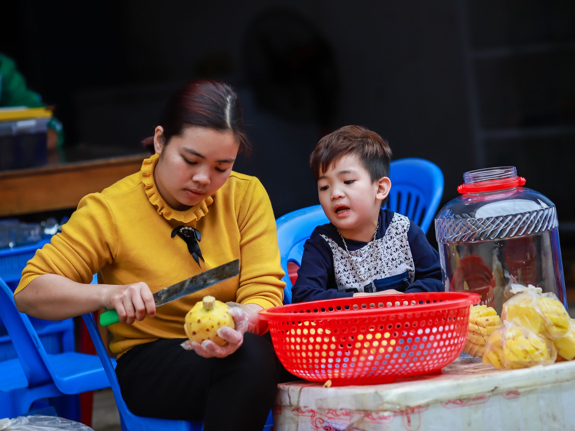 An adult and child peeling fruit outdoors at a market in Lào Cai, Vietnam.