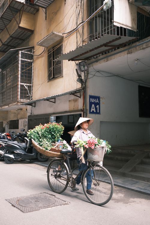 Free Woman selling flowers on a bicycle in a bustling urban street, showcasing local culture. Stock Photo