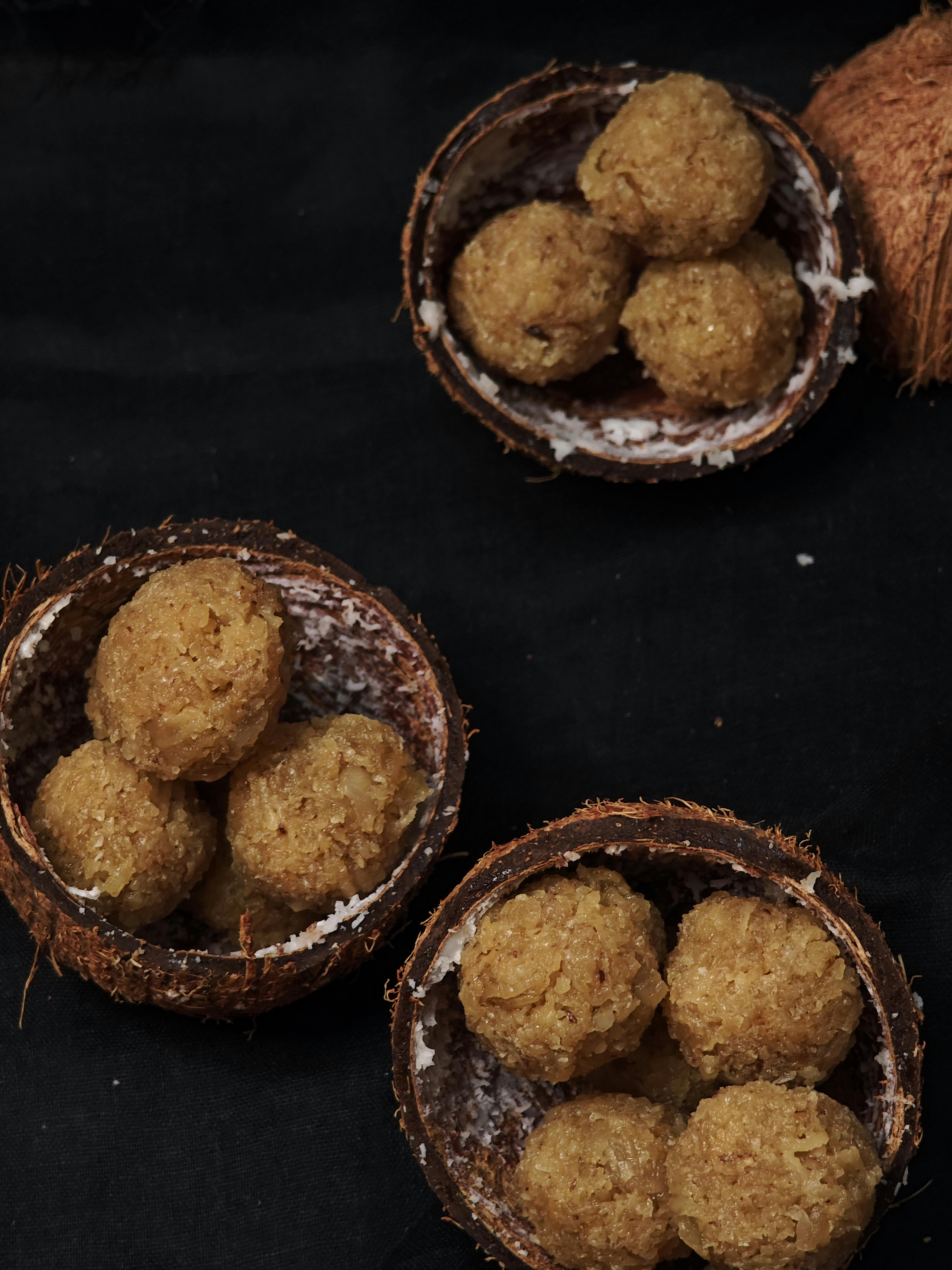 Tasty coconut ladoo served in coconut shells on dark background.
