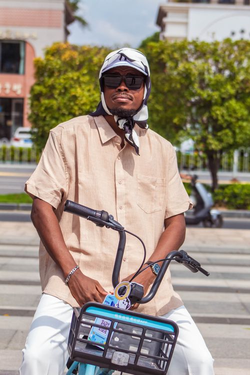 Free A fashionable man in sunglasses rides a blue bicycle on a sunny city street. Stock Photo