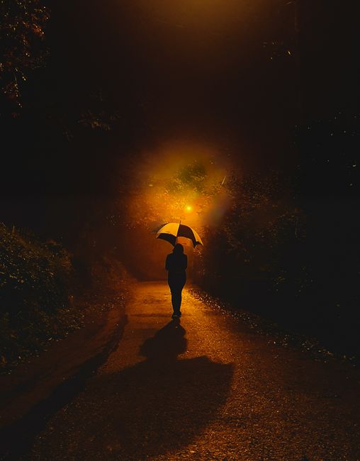 Mysterious silhouette walking under streetlight at night with an umbrella casting shadows.
