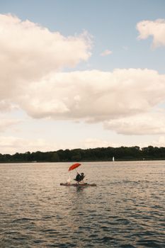 A couple paddles on a serene lake with an umbrella, surrounded by nature in Werder, Germany.