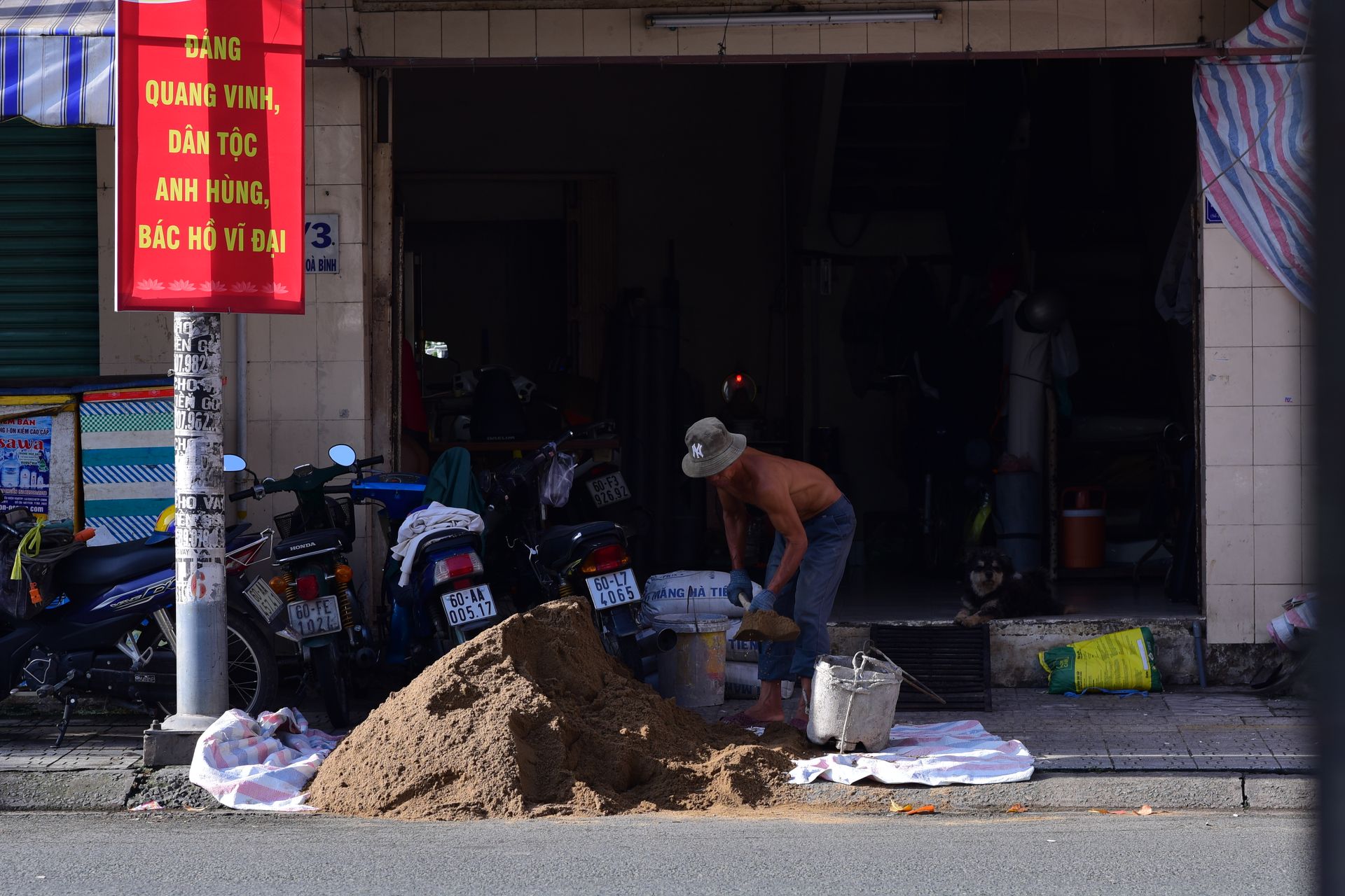 A construction worker piles sand outside a shop on a busy street in Vietnam, surrounded by motorbikes.