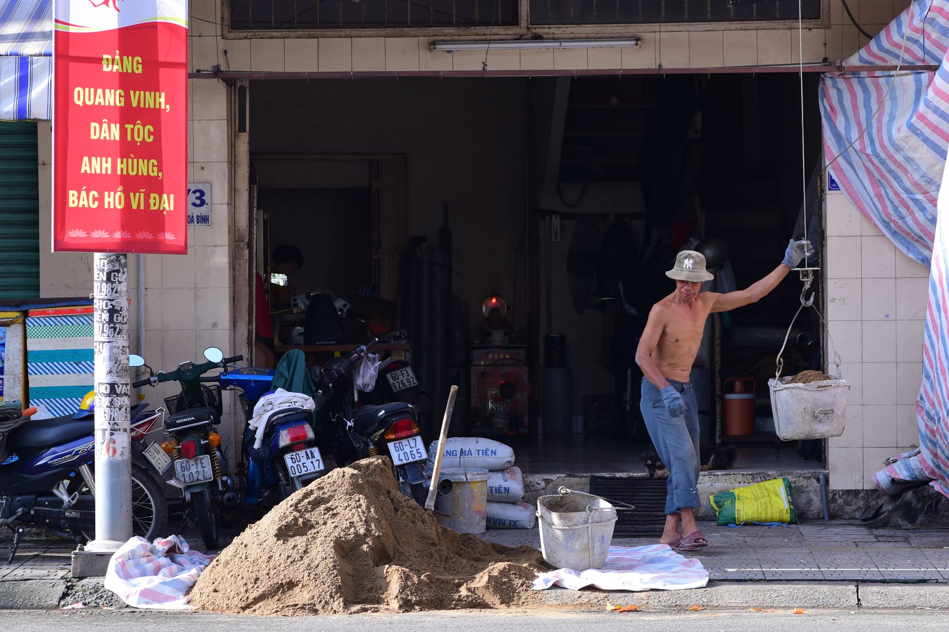 A construction worker lifting materials in an urban street setting. Vibrant day scene with bystander and motorbikes.