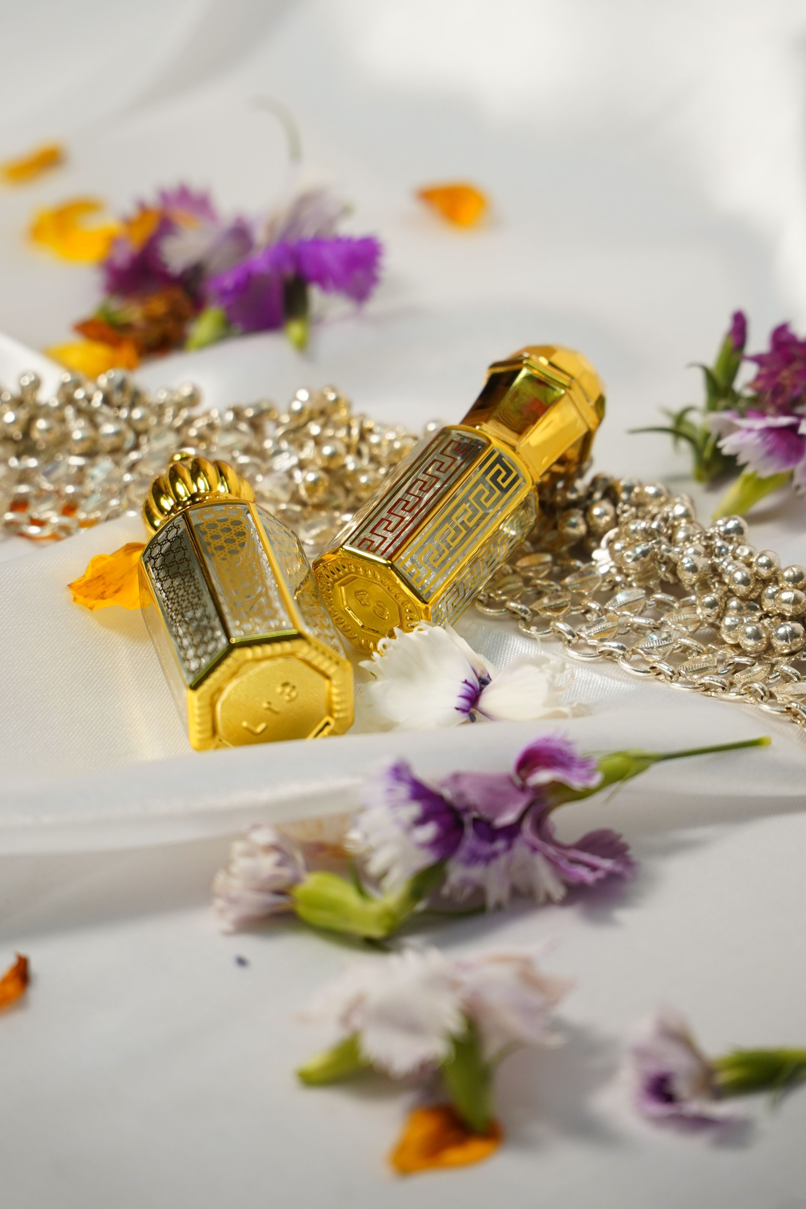 Gold perfume bottles artfully displayed with flowers and beads on a white fabric.