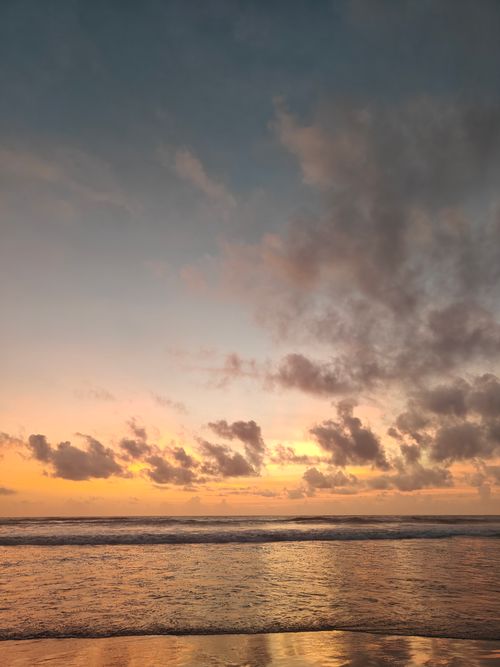 Free A beautiful beach sunset with vibrant clouds reflecting off calm ocean waters. Ideal for relaxation themes. Stock Photo