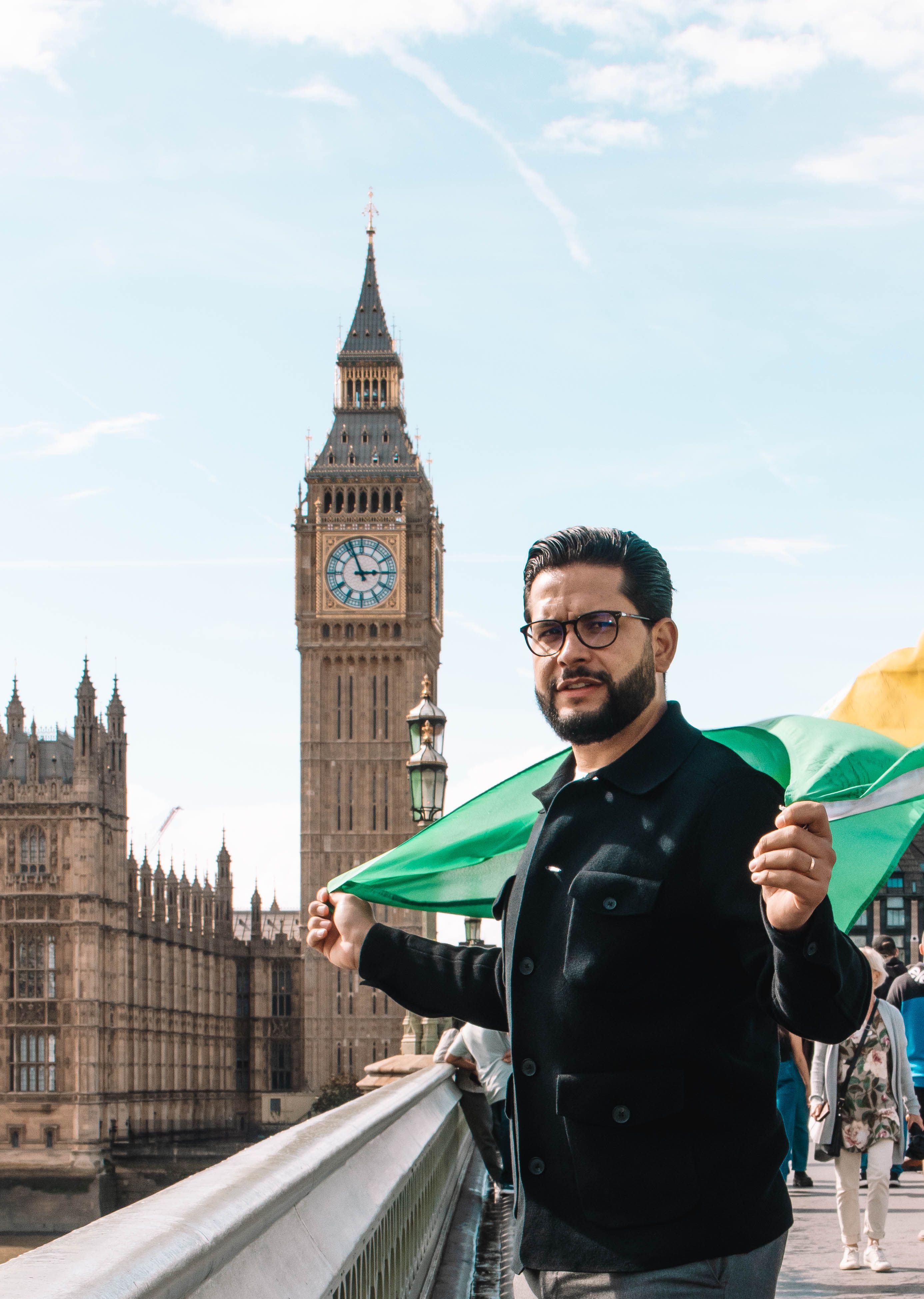 Man with flag poses in front of the iconic Big Ben in London, perfect for travel themes.