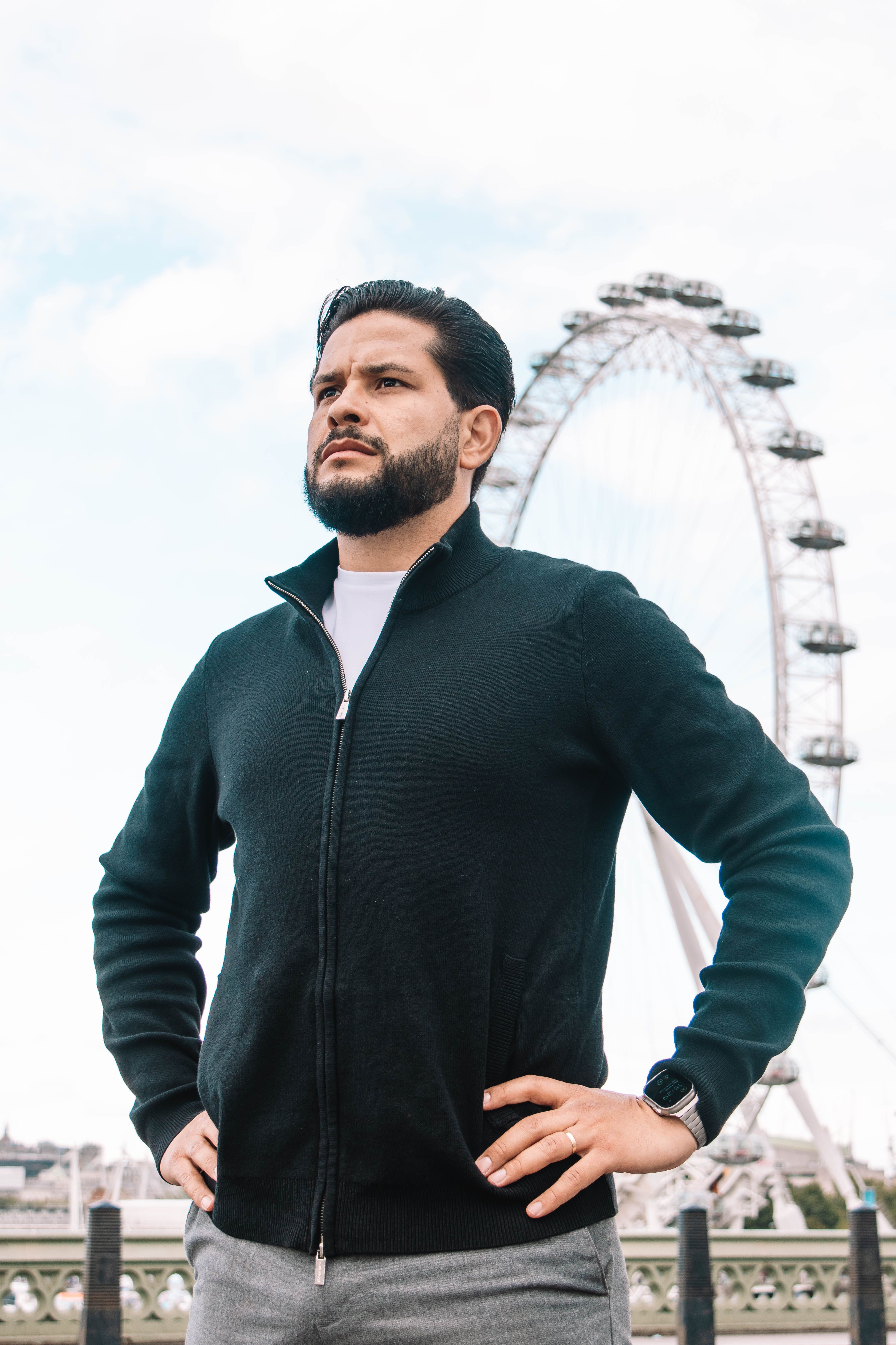 A man stands confidently with hands on hips, London Eye in the background.