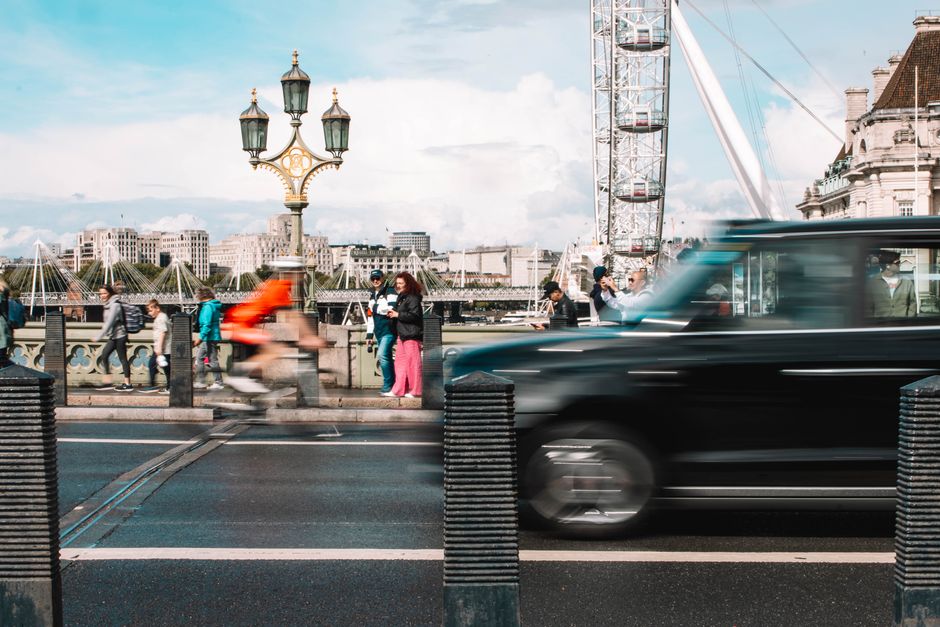 A bustling city street in London featuring pedestrians, a cyclist, a taxi, and the iconic London Eye.