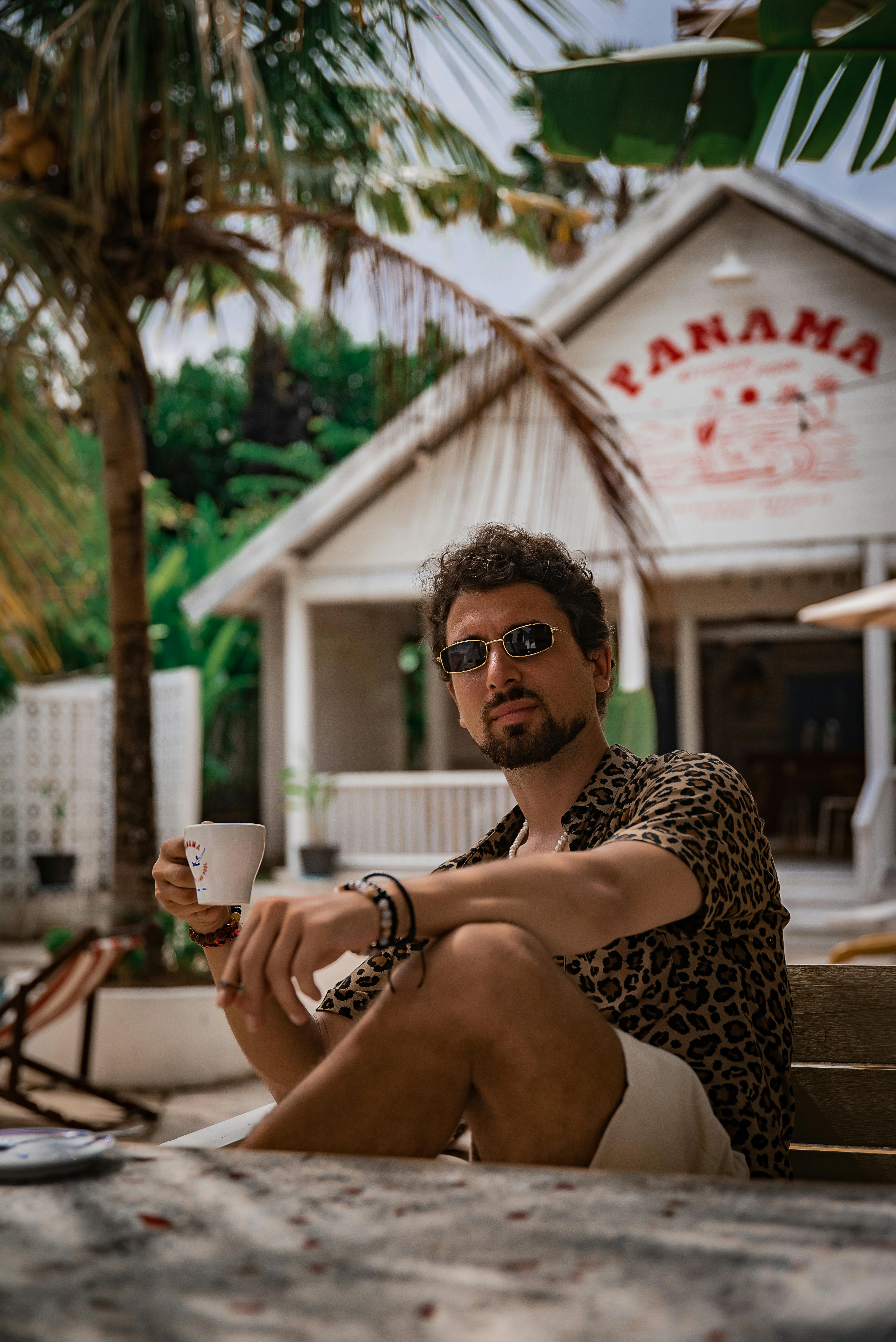 Free A man in sunglasses and leopard shirt enjoying coffee outdoors at Panama Cafe in Bali. Stock Photo