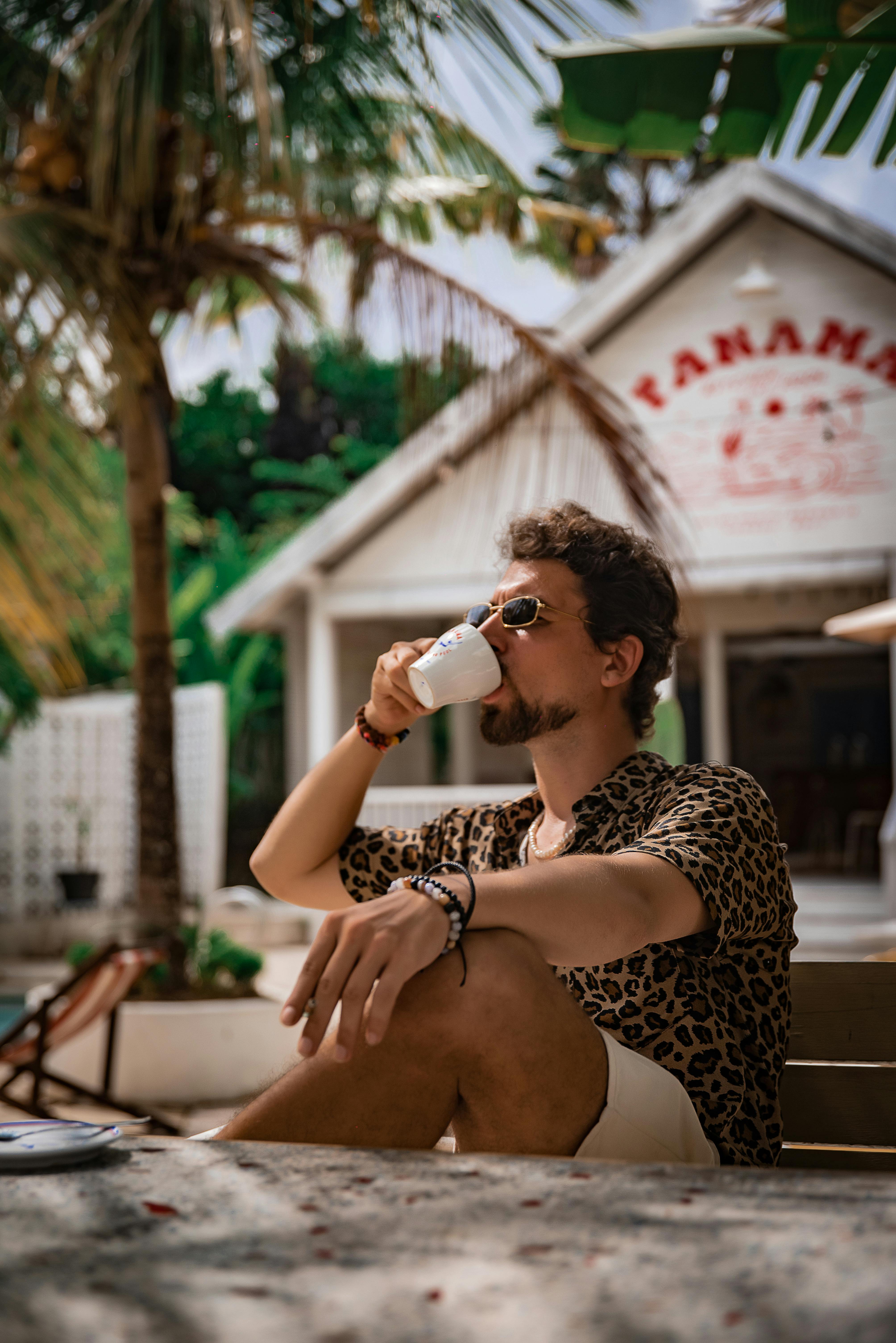 Free Man sipping coffee at a tropical cafe in Bali, Indonesia, surrounded by palm trees. Stock Photo