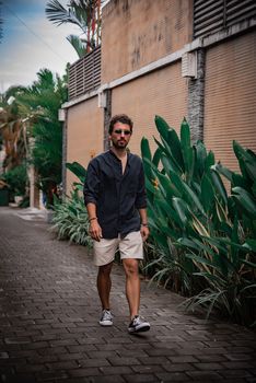 Casually dressed man walking on a cobblestone street surrounded by tropical plants in Bali.