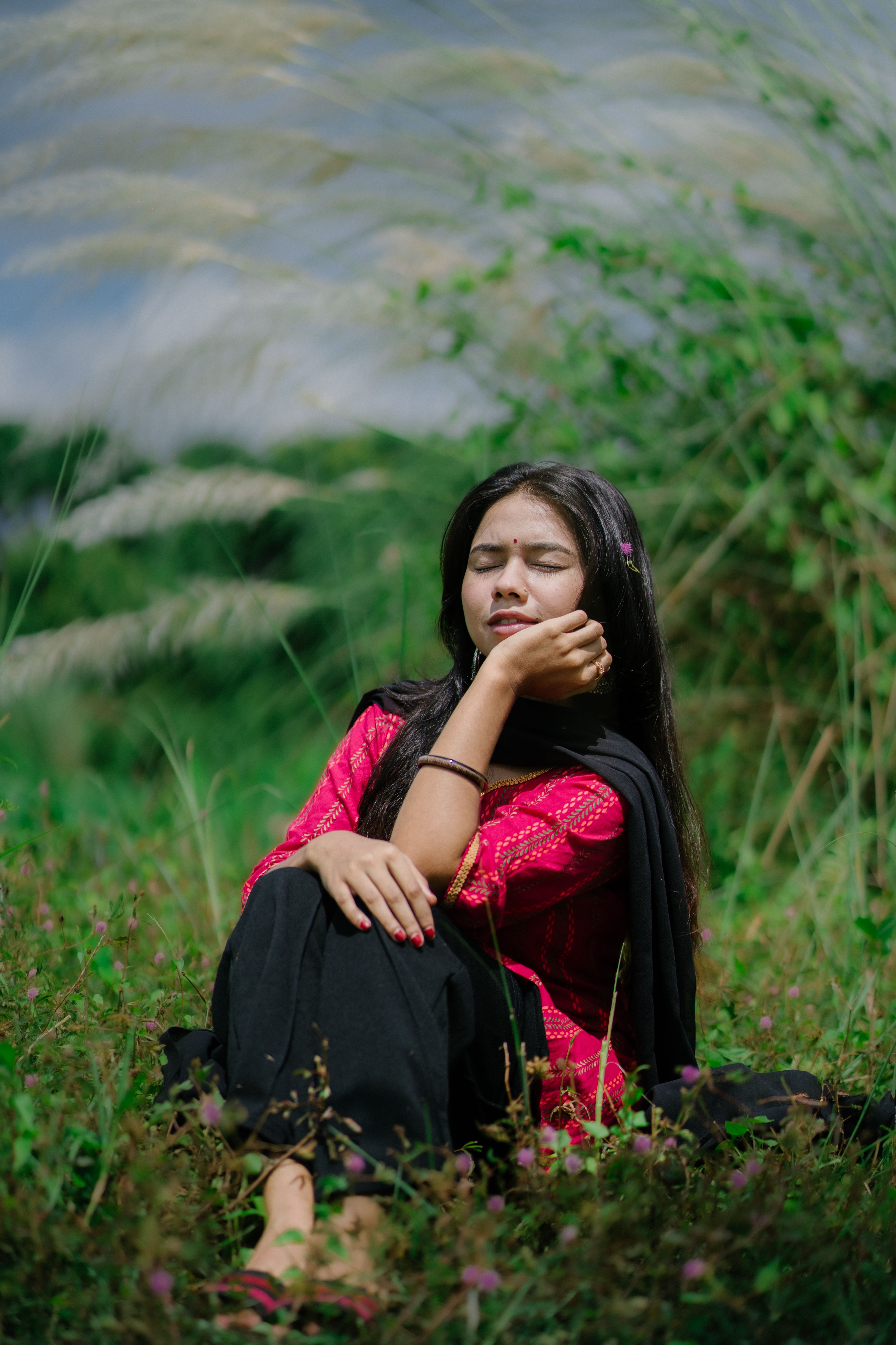 A peaceful moment with a woman in traditional attire relaxing in a vibrant green field.