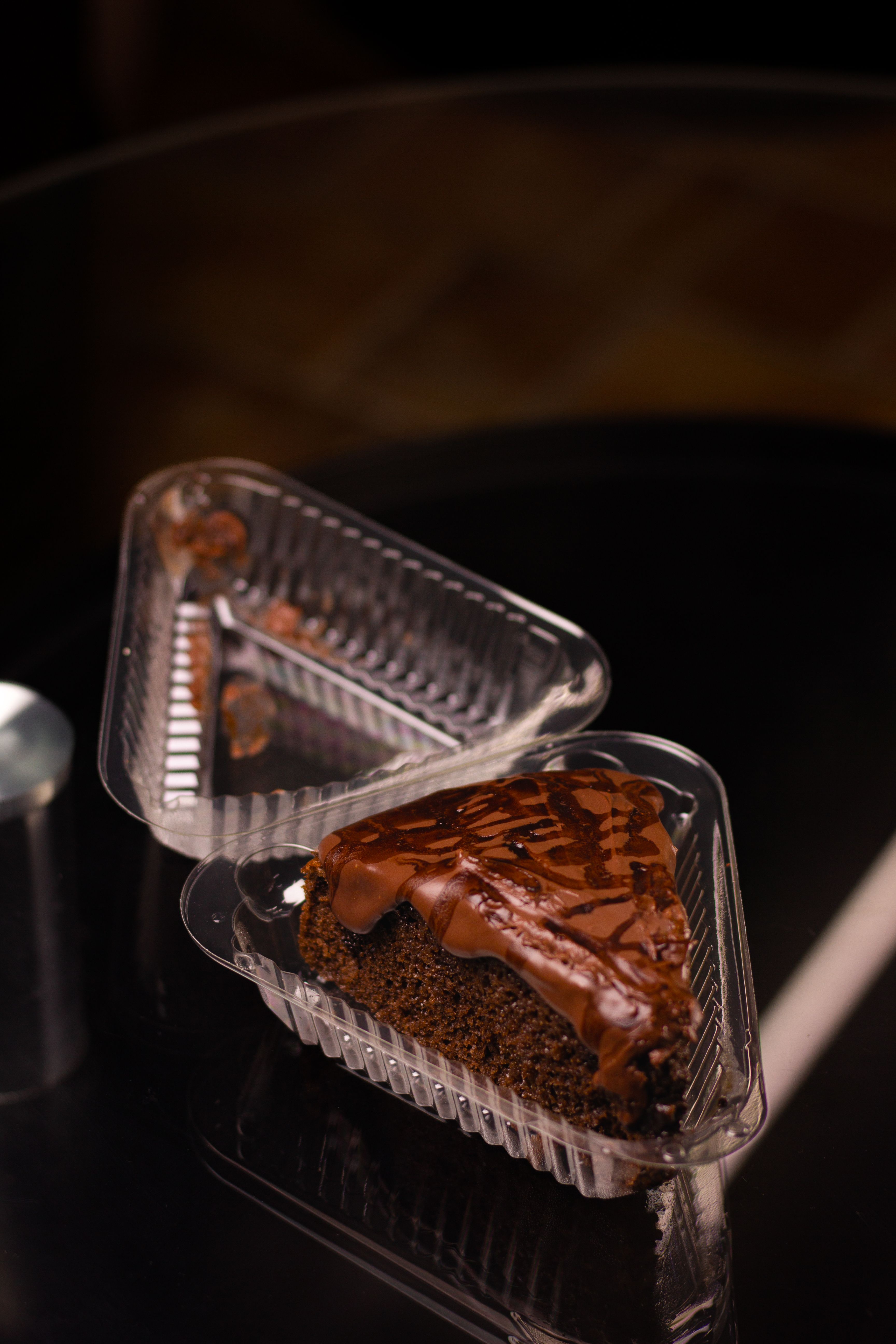 Indulgent slice of chocolate cake with drizzle captured in a plastic container on dark surface.