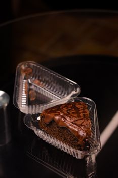 Indulgent slice of chocolate cake with drizzle captured in a plastic container on dark surface.