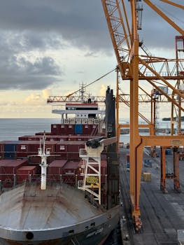 Dynamic view of a bustling port with container ship and cranes during the day.