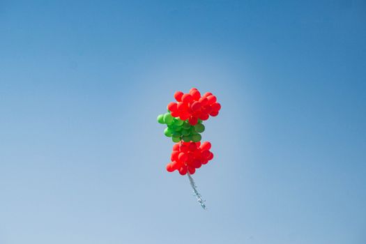 Red and green balloons soar against a clear blue sky, symbolizing freedom and celebration.