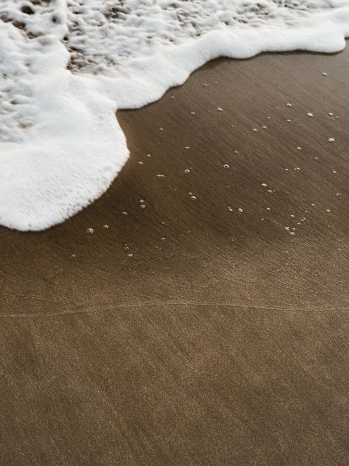 Free Close-up of ocean wave foam gently washing over sandy beach shore texture. Stock Photo