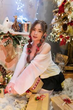 Young woman with gifts by a decorated Christmas tree and festive lights.