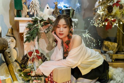 Young woman in festive setting, surrounded by holiday decor and lights, evoking a warm Christmas atmosphere.