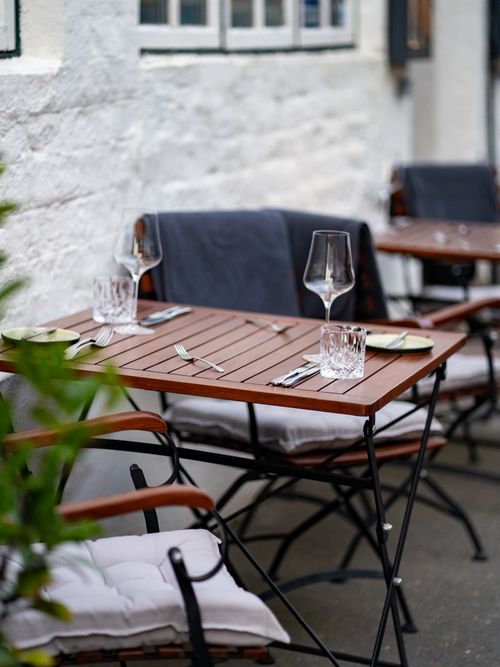 Free Elegant outdoor cafe setup with wooden table and cushioned chairs, perfect for dining. Stock Photo