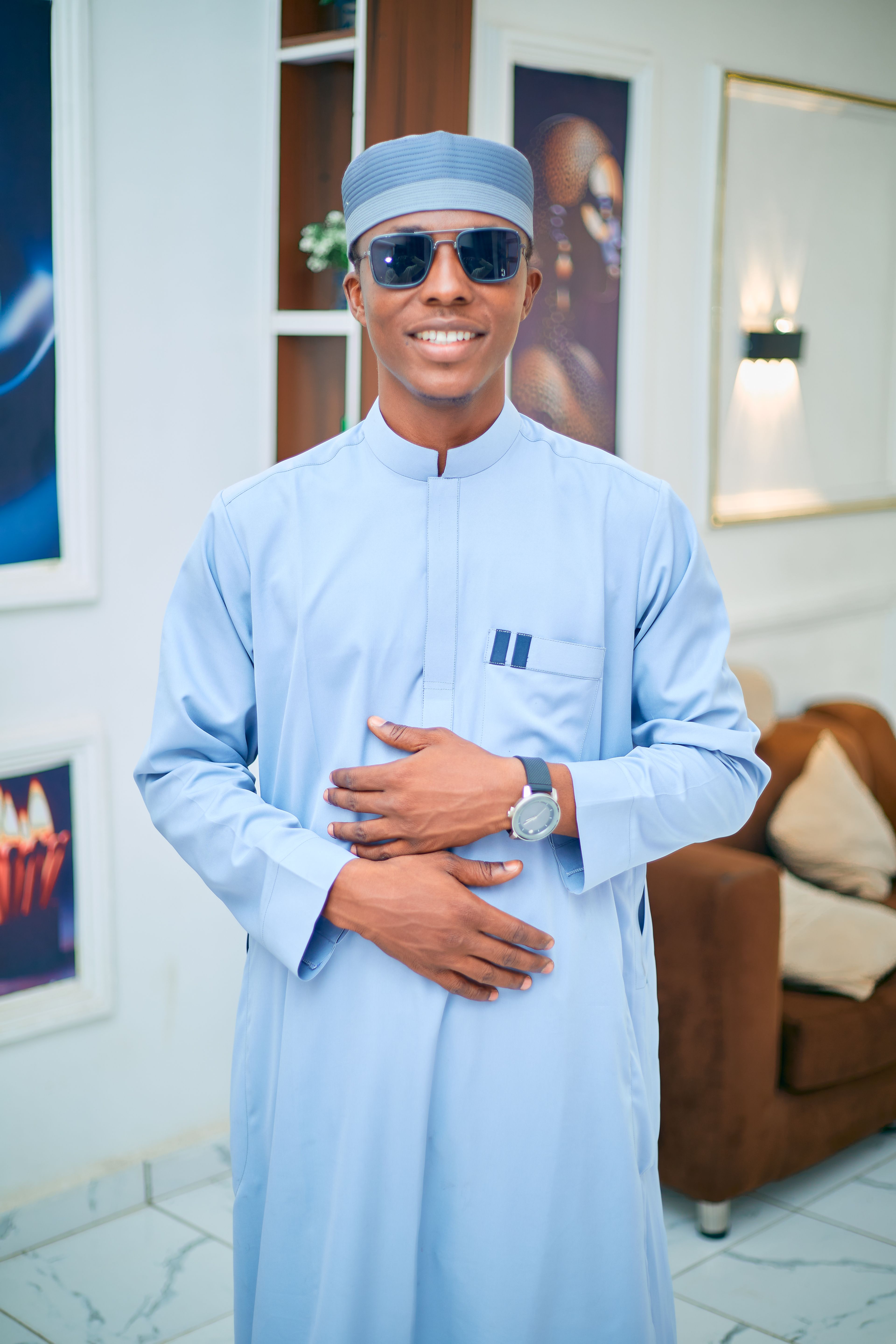 Confident man wearing blue traditional attire and sunglasses, smiling indoors.