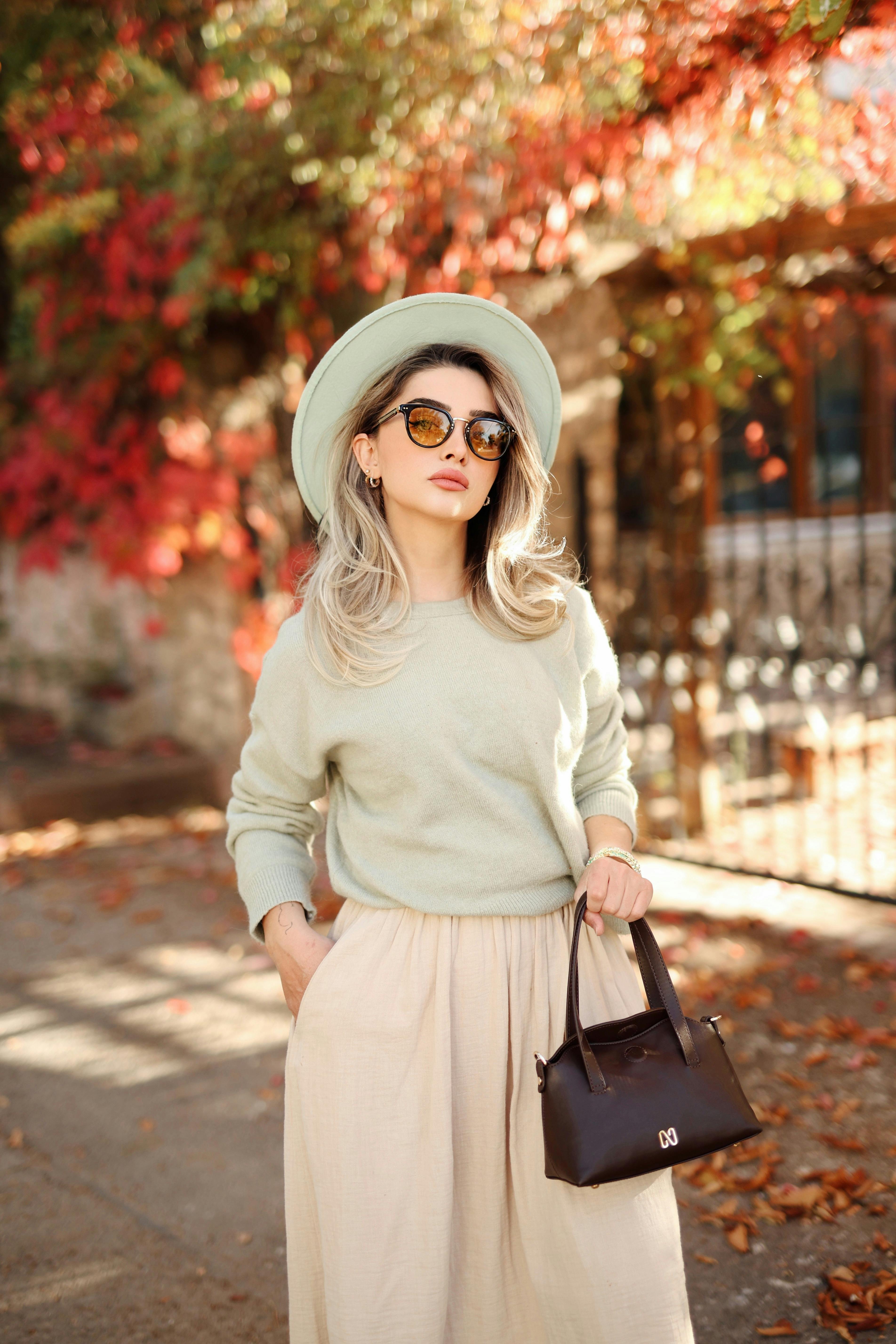 Fashionable woman in autumn attire posing outdoors with red foliage.