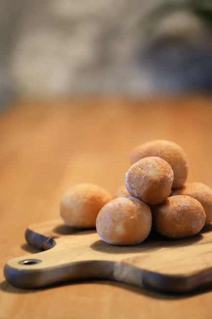 A red plastic bucket overflowing with mini donut holes coated in cinnamon-sugar, vanilla glaze, and chocolate glaze, spilling onto a wood table.