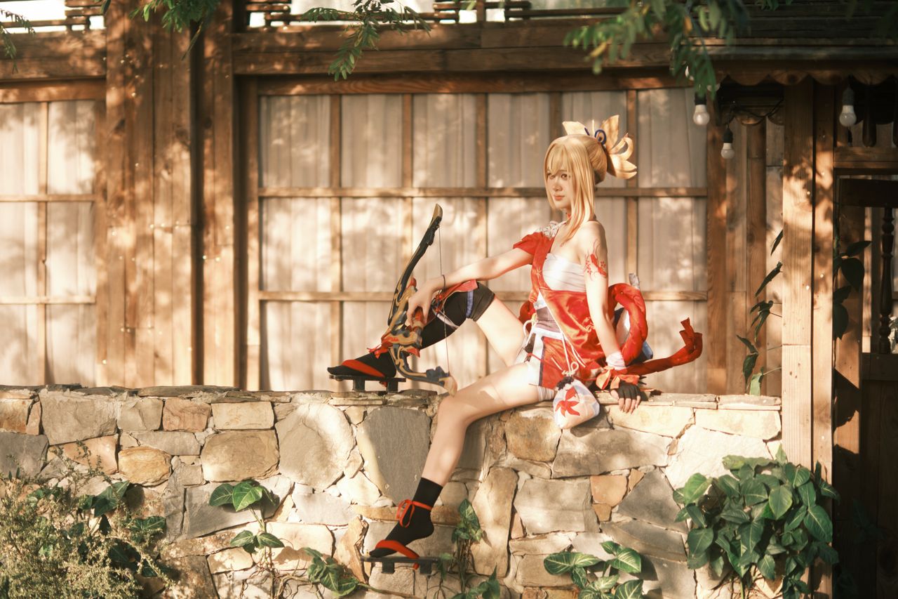 a female cosplayer sits on a stone wall holding a bow in front of a wo