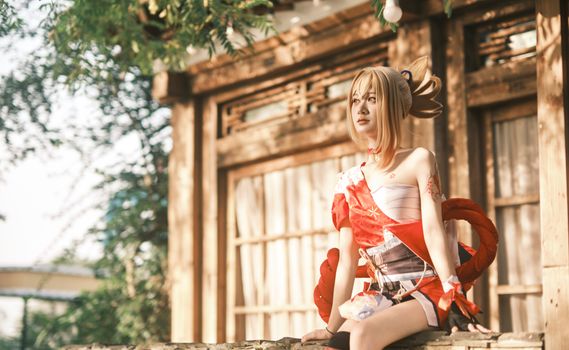 A cosplayer dressed in traditional Japanese attire sits thoughtfully outdoors, capturing a serene moment.