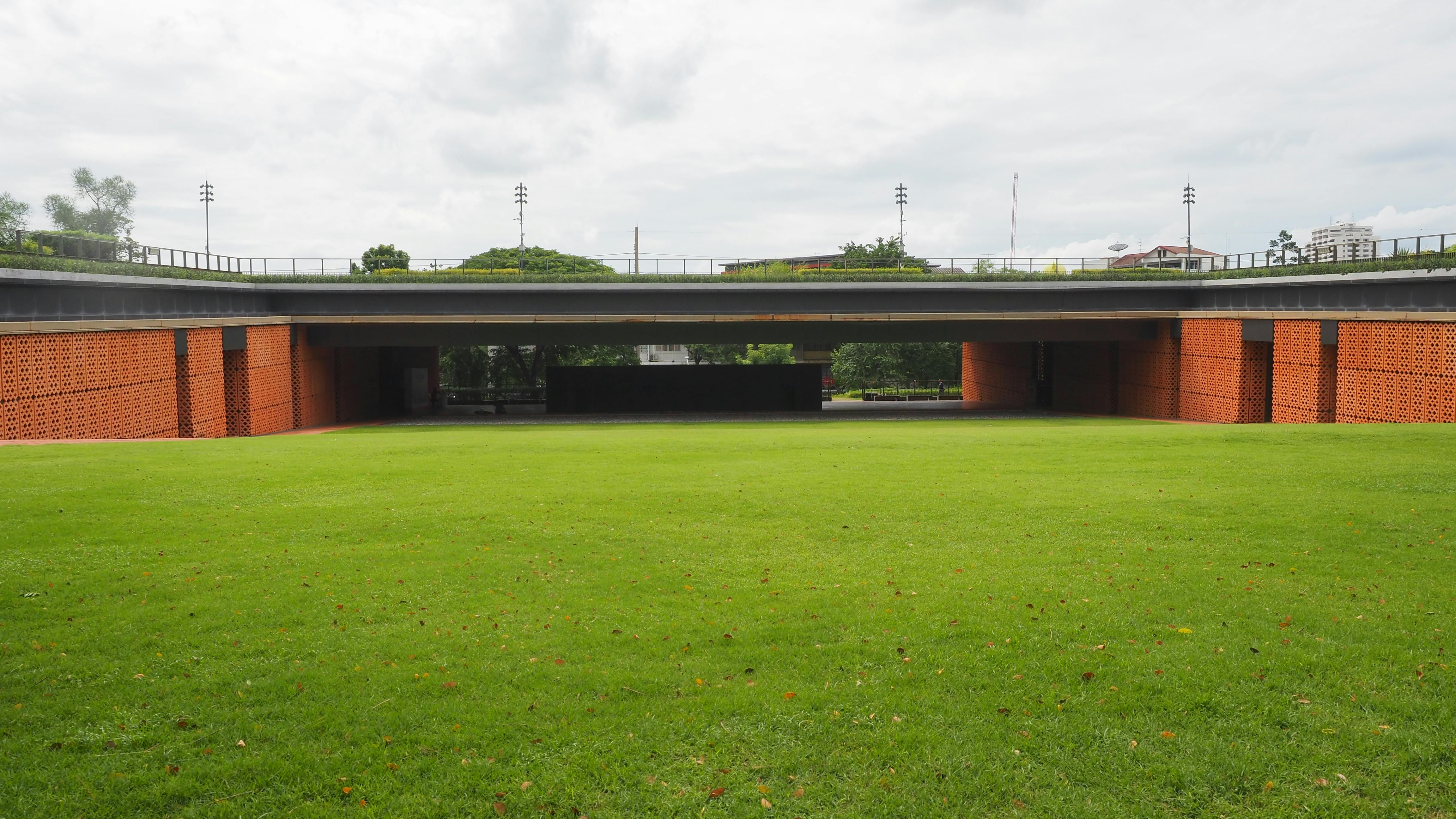 Imagem de um espaço aberto com grama bem cuidado sob uma ponte, ideal para ilustrar temas de sustentabilidade e urbanismo verde.