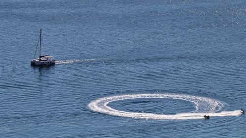 Free A sailboat and jetski create dynamic patterns on the blue ocean. Stock Photo