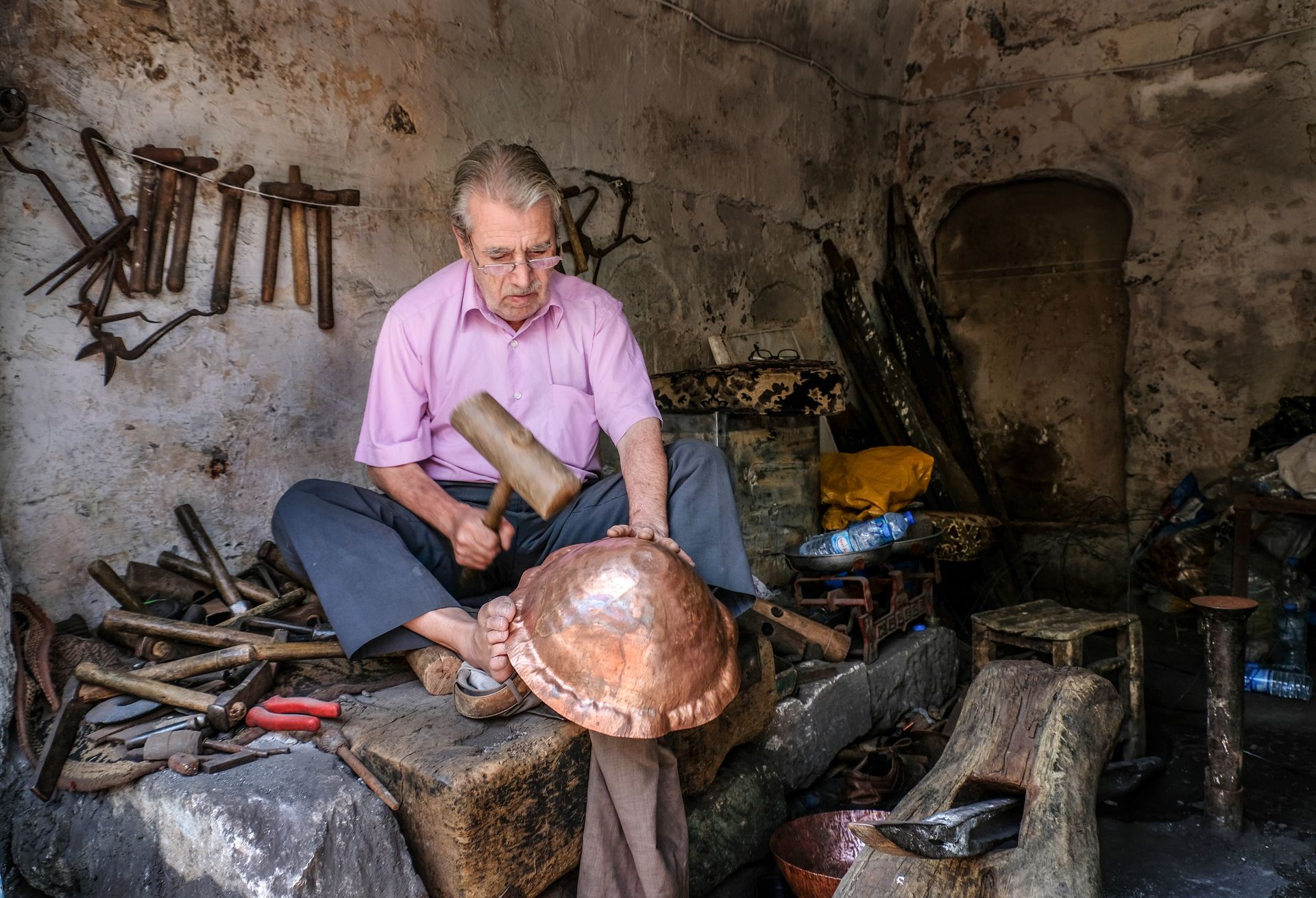 An artisan skillfully works on a copper bowl using traditional tools in an old workshop.