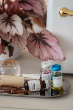 Elegant arrangement of skincare bottles and pink leaves on a reflective tray, capturing a modern aesthetic.