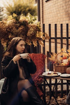 A woman enjoying coffee outdoors in an autumn setting with a basket and treats.
