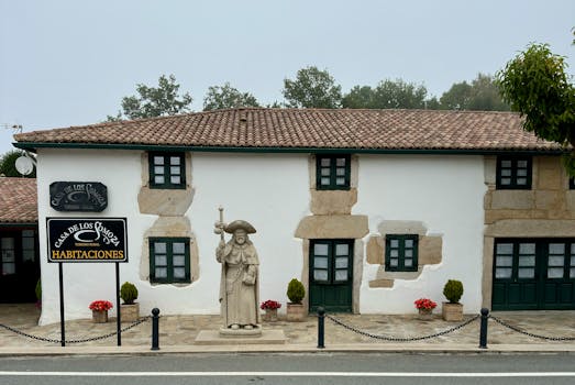 Cozy rural house with stone facade and historic statue in a quaint setting.