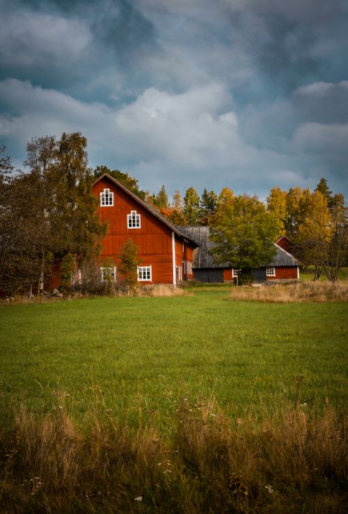 Free A picturesque red barn surrounded by lush green fields and fall foliage under a dramatic sky. Stock Photo