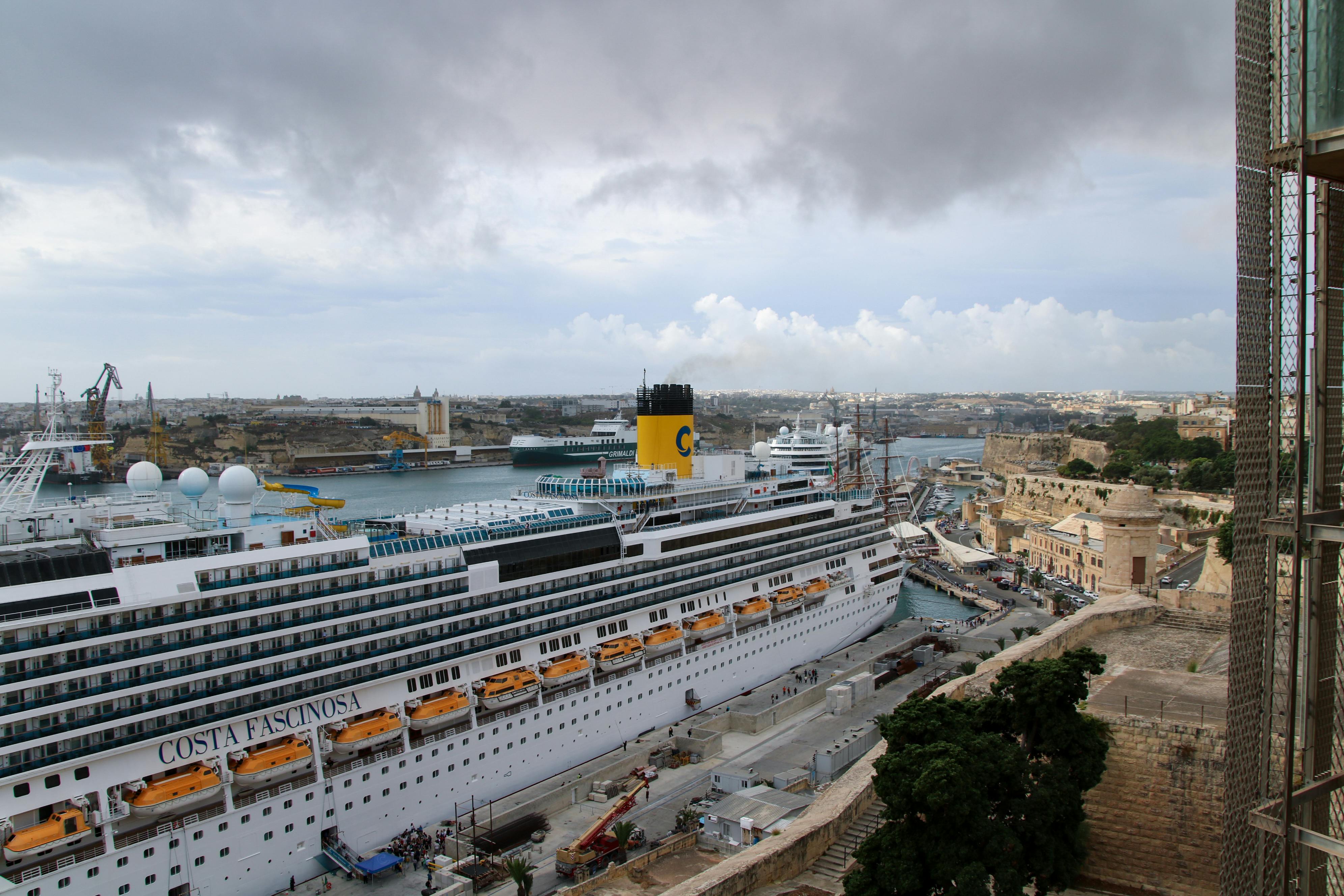 Aerial view of a large cruise ship docked at La Valletta port, Malta, with overcast skies.