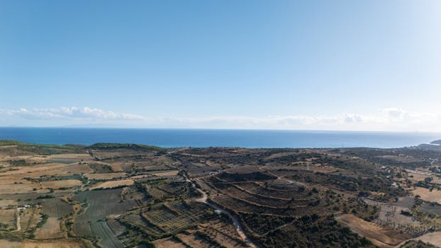Stunning aerial view of a coastal landscape featuring lush fields, sea, and clear sky.