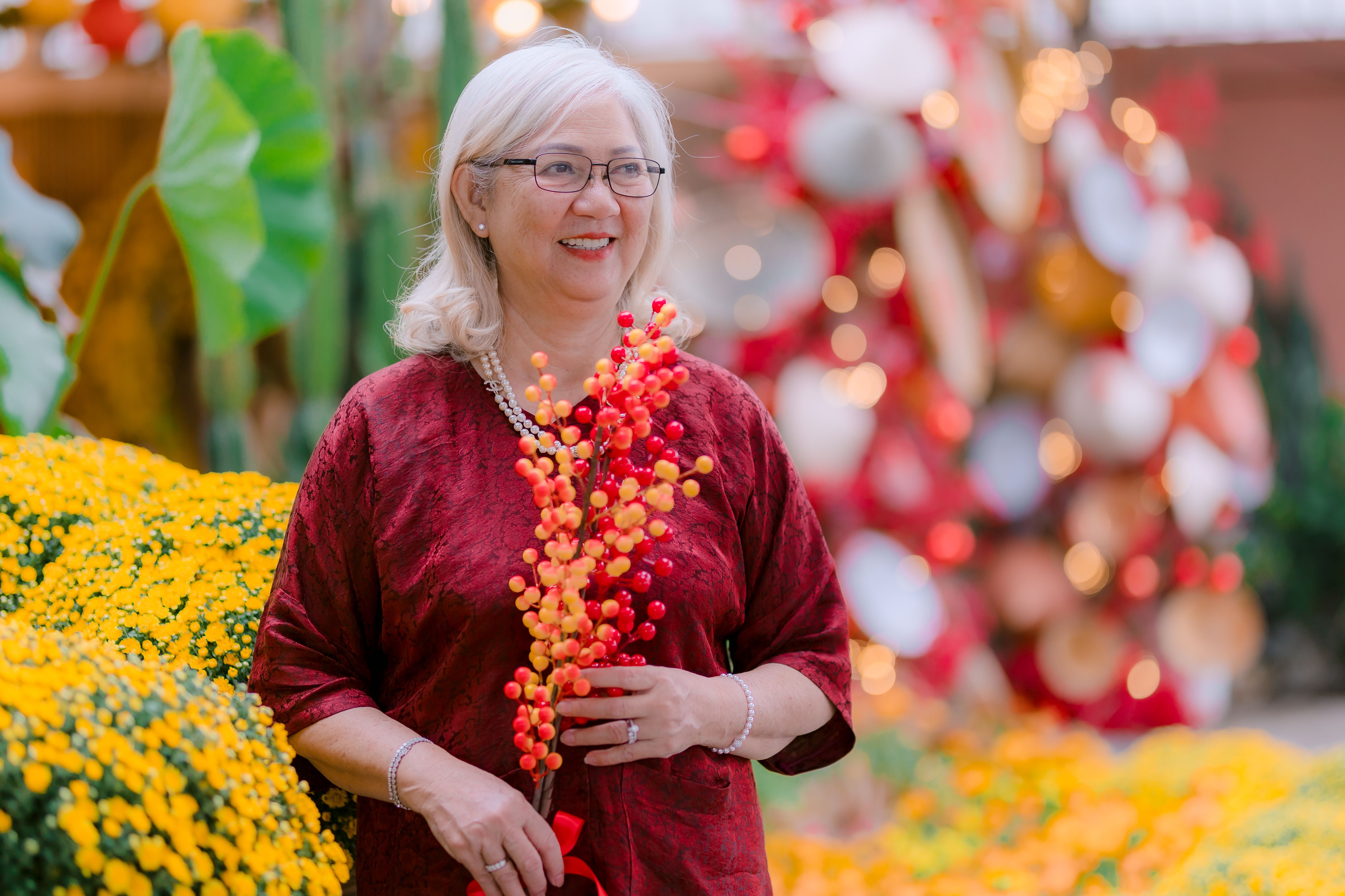 Senior woman in red enjoying a festive garden setting with bright flowers.