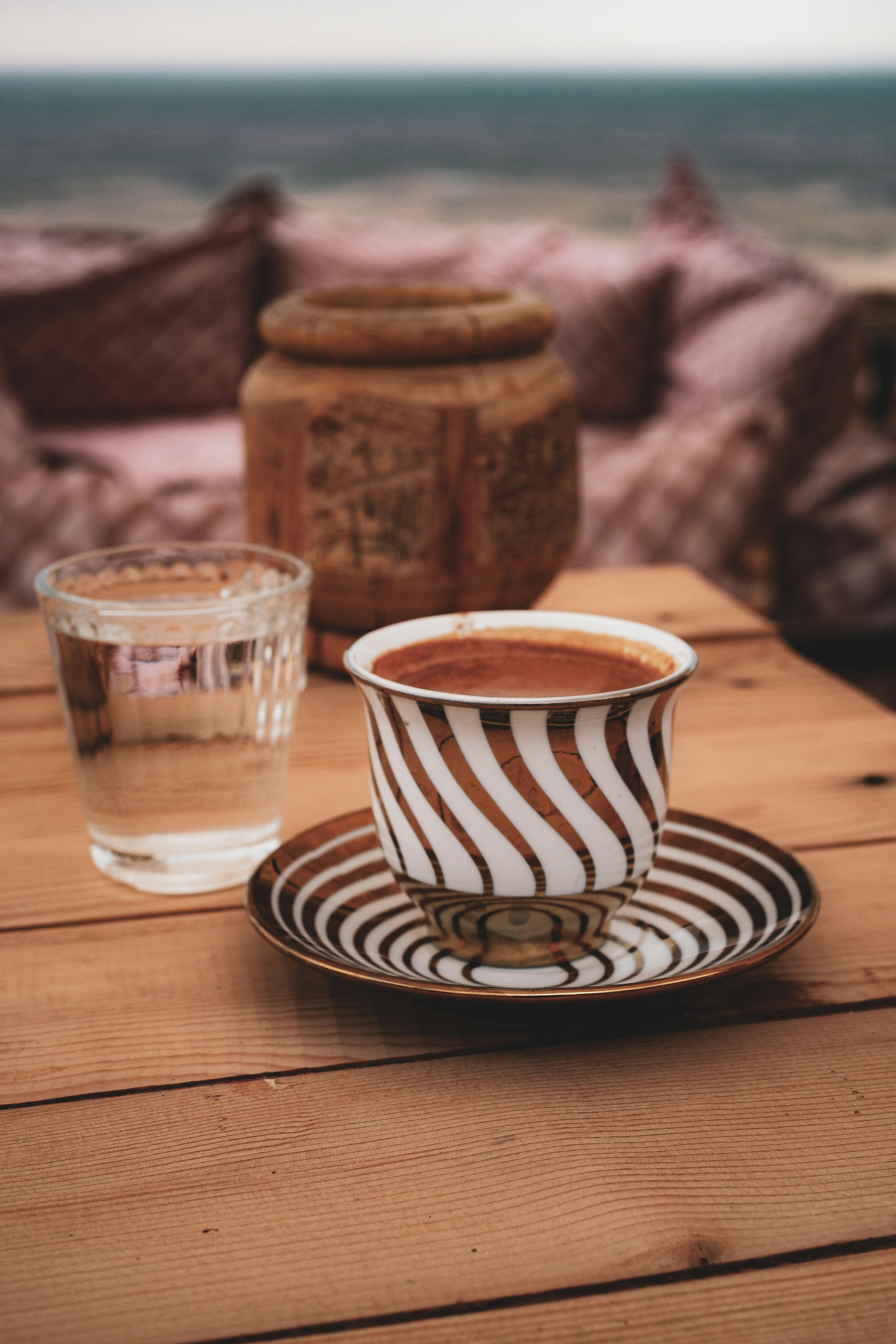 Elegant coffee setup with chic cup and glass on a wooden table in an outdoor setting.