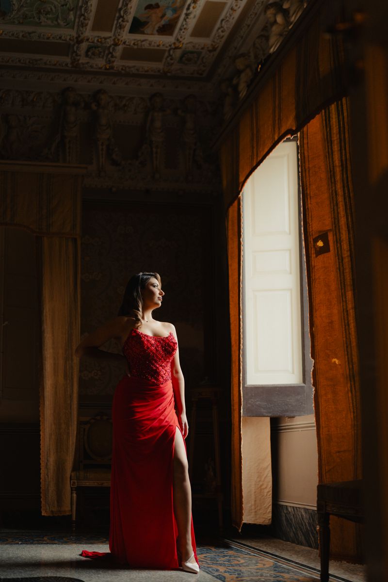 Woman in a red gown posing by an ornate window