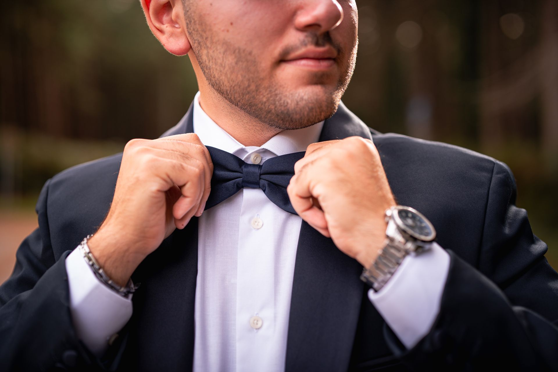 Close-up of a man adjusting a bow tie, showcasing elegance and fashion in an outdoor setting.