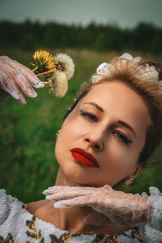 Portrait of a stylish woman outdoors, holding dandelions, wearing bold red lipstick and lace gloves.