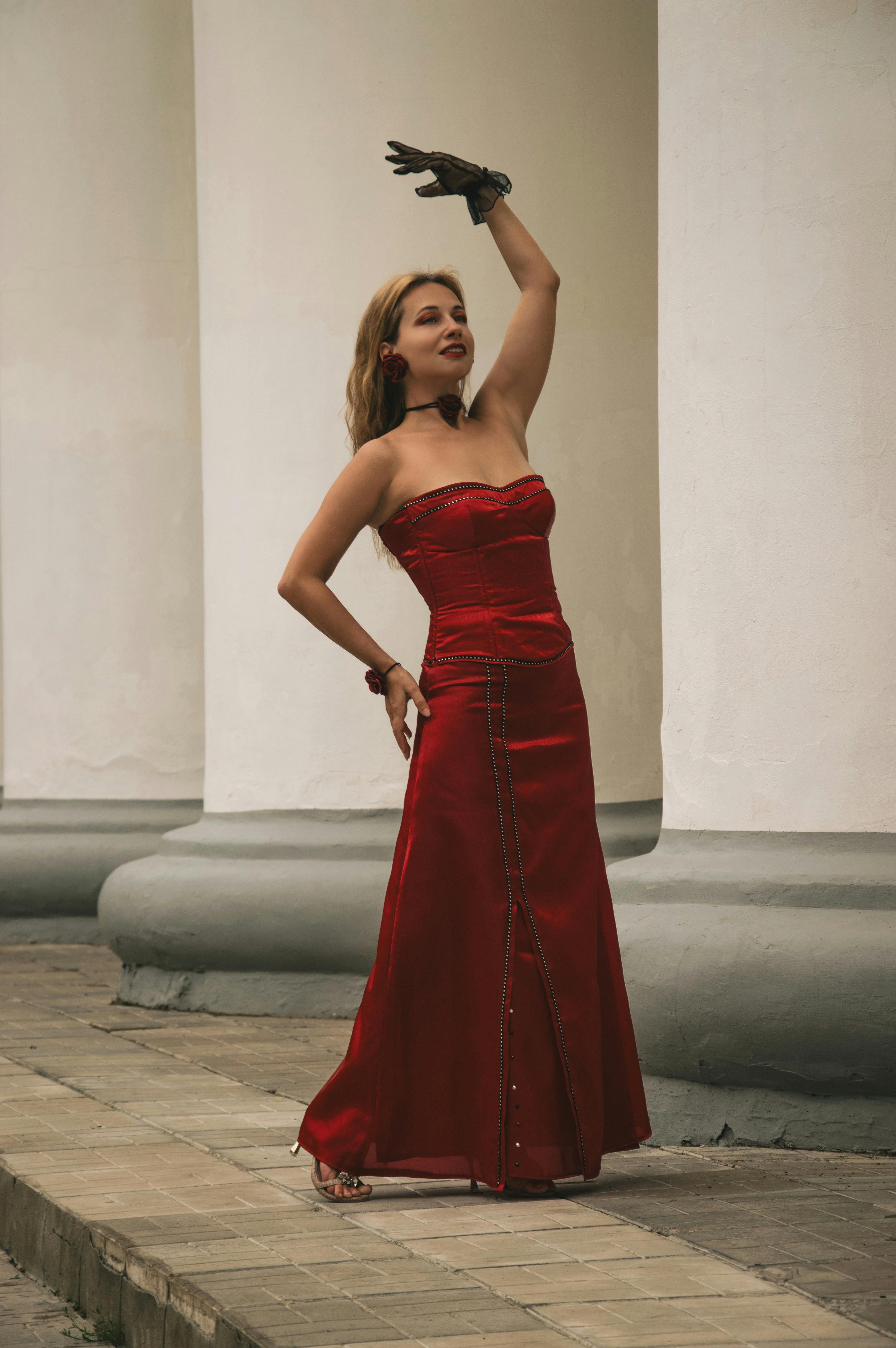 一个穿着红色晚礼服的女人优雅地靠在柱子上，散发出优雅和风格